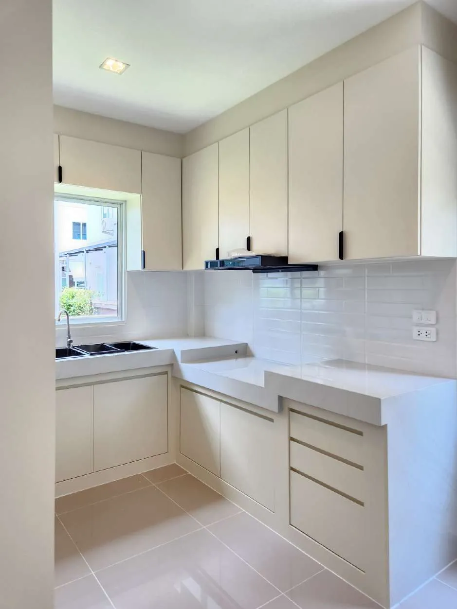 Finished white kitchen with handleless cabinets, stone counters and a window over the sink